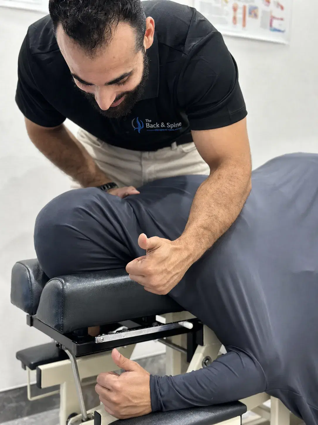 Dr Laith Musallam leaning over a patient lying on a drop table, both hands set on the lower back.