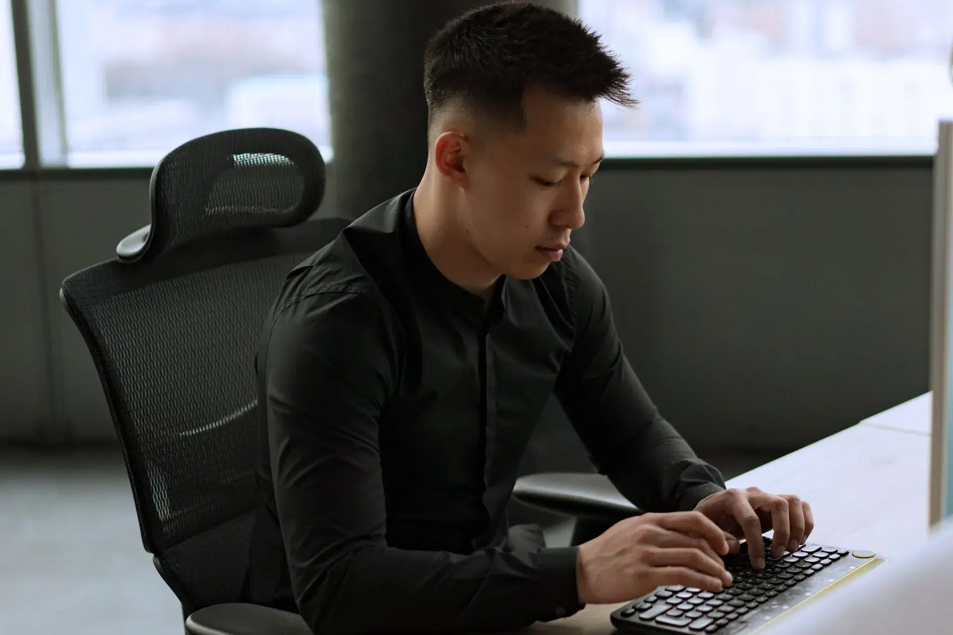 An office worker typing at a monitor, head carried forward of the shoulders.