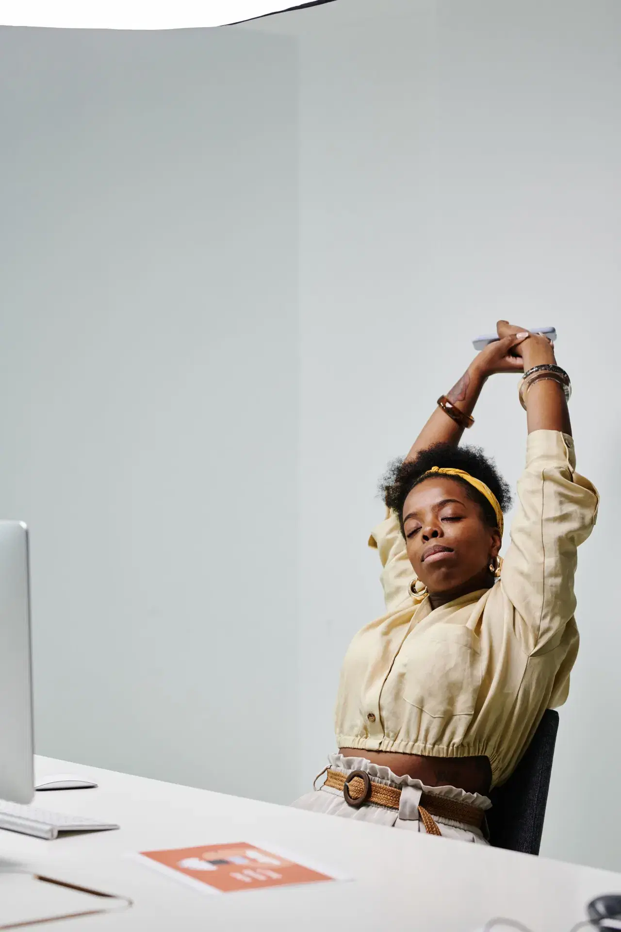 A woman at a desk with her arms locked overhead, extending backwards over the chair.