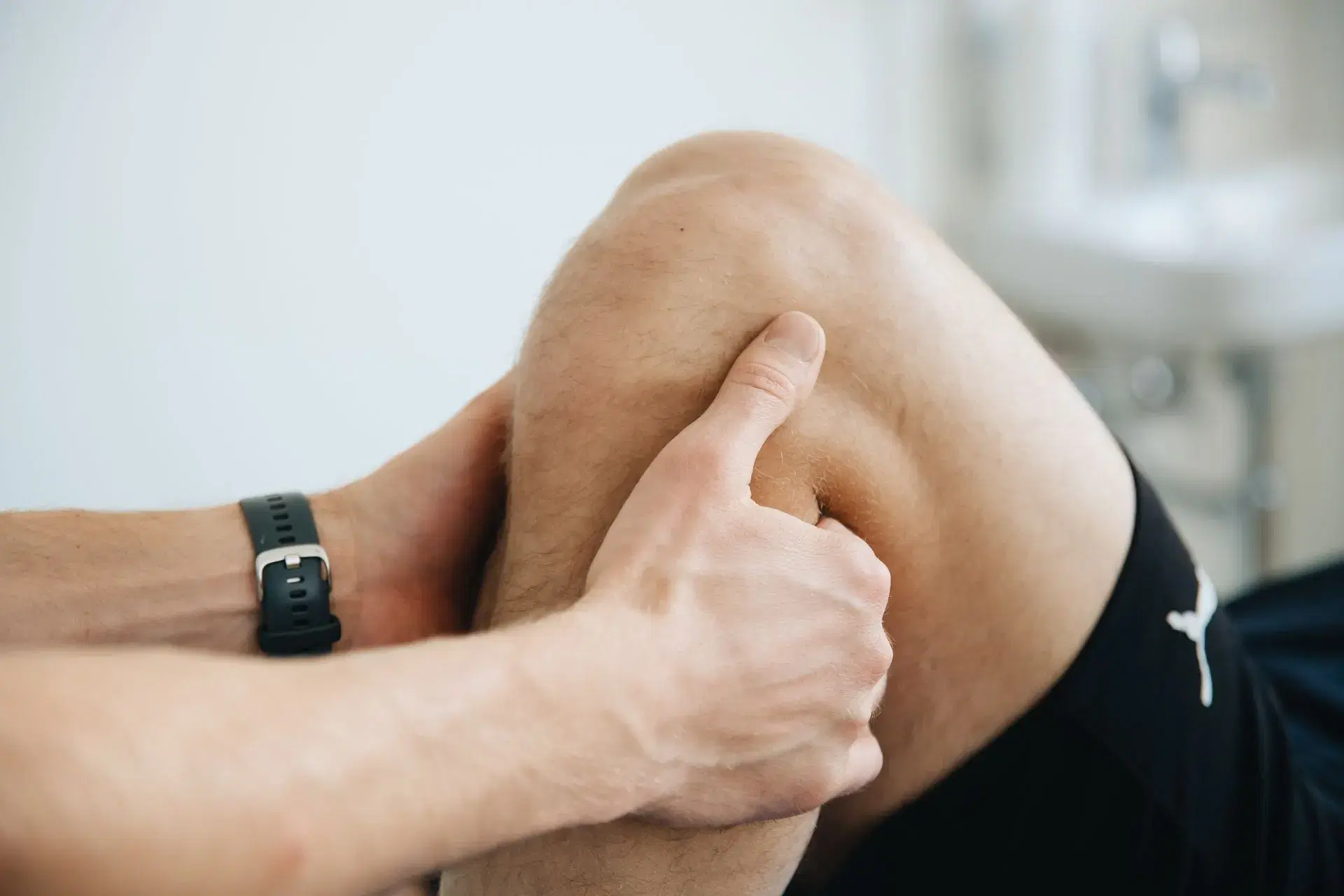 A close crop of two hands working a bent knee, one thumb pressed into the joint line.