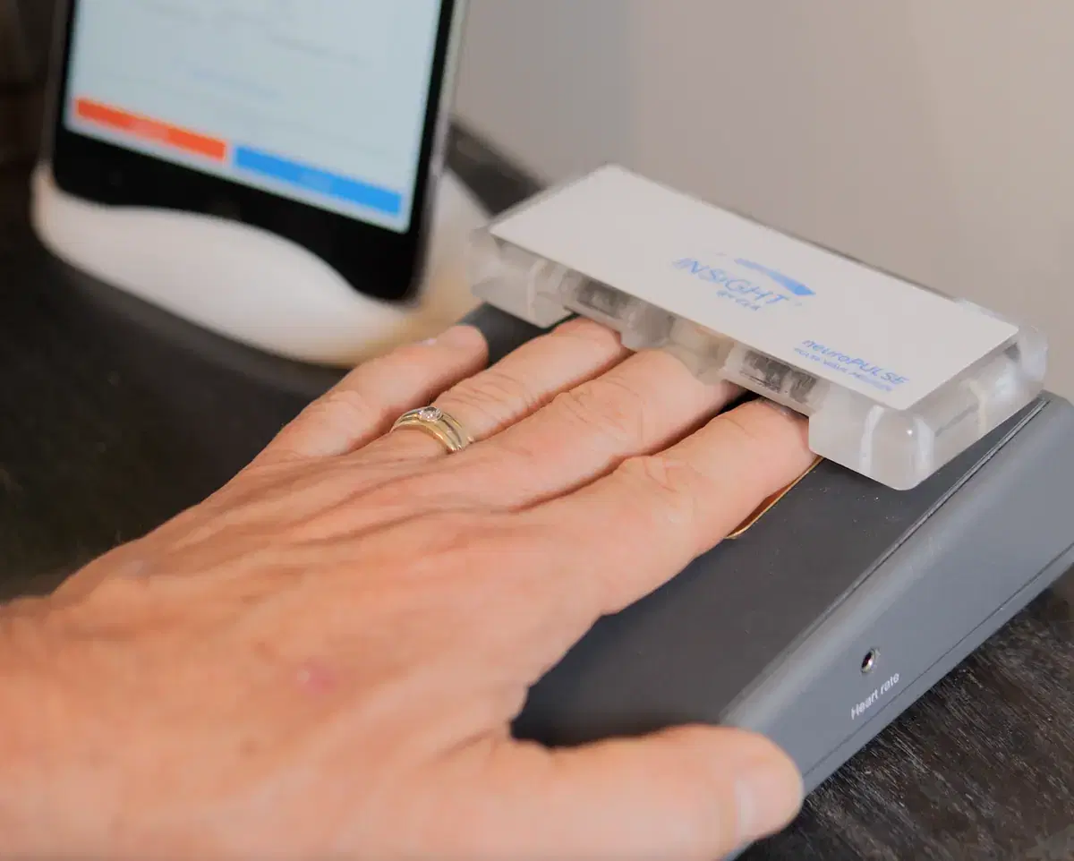 A patient resting a hand on the NeuroPULSE sensor during a scan.