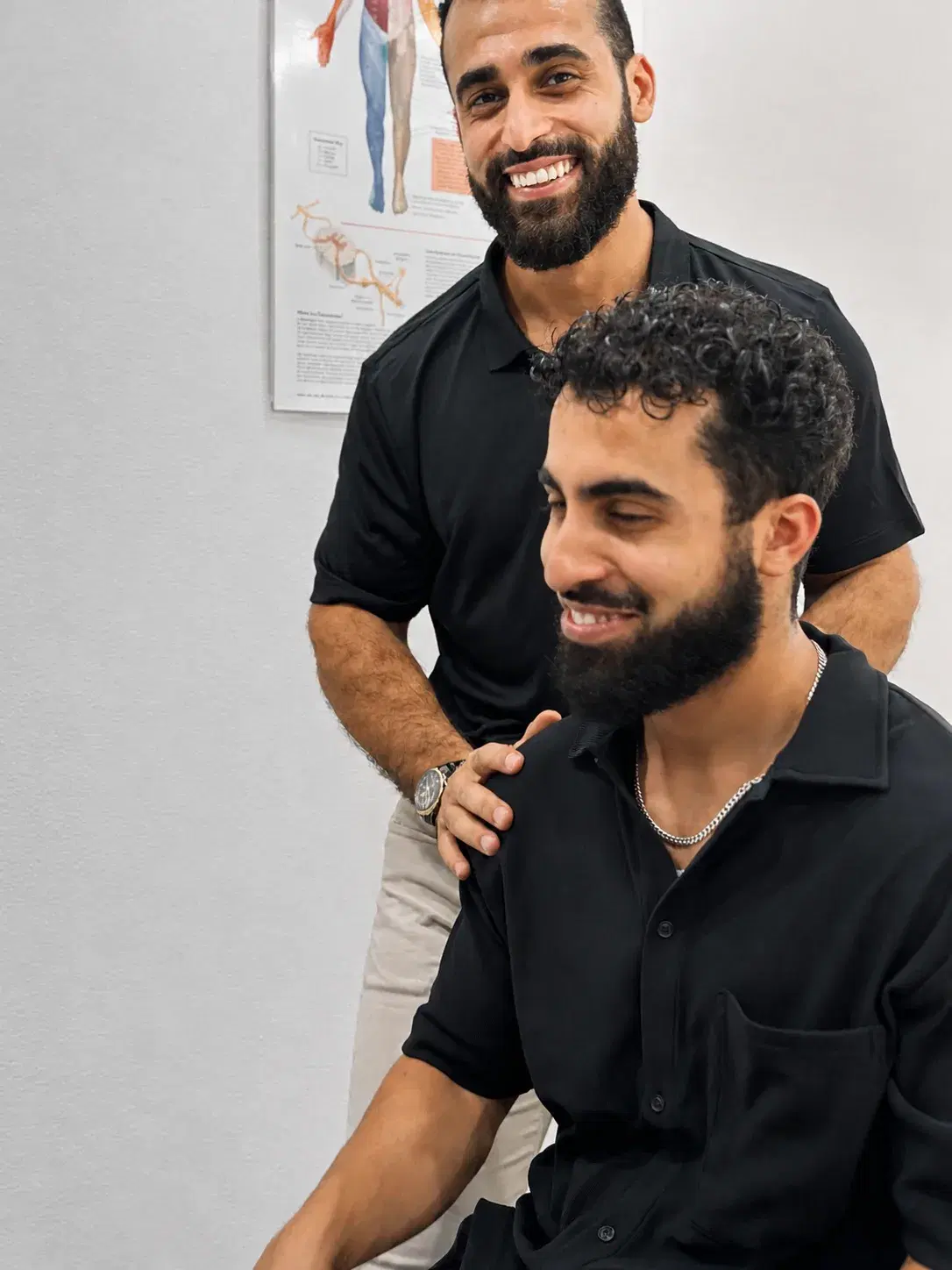 Dr Laith Musallam standing behind a seated patient with a hand on their shoulder, both of them smiling.